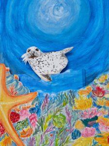 Praca plastyczna przedstawiająca fokę płynącą w błękitnej wodzie nad kolorową rafą koralową z dużą, pomarańczową rozgwiazdą na pierwszym planie.