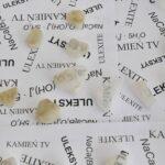 Małe kawałki jasnego minerału, uleksytu, ułożone na białych kartkach z wydrukowanymi nazwami „kamień TV”, „uleksyt” oraz wzorem chemicznym tego minerału.