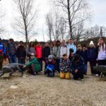 Grupa uczniów pozuje do wspólnego zdjęcia, stojąc obok dwóch metalowych rzeźb prehistorycznych gadów.