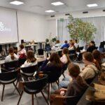 Uczniowie siedzą w sali wykładowej przed ekranem z logo „GEOsfera”, a obok nich, na pierwszym planie, widoczna jest ekspozycja dużych kości i skamieniałości.